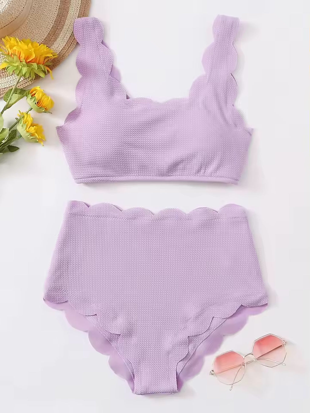 Lavender textured bikini with scalloped edges and ruched crop top displayed flat lay with straw hat and sunglasses.