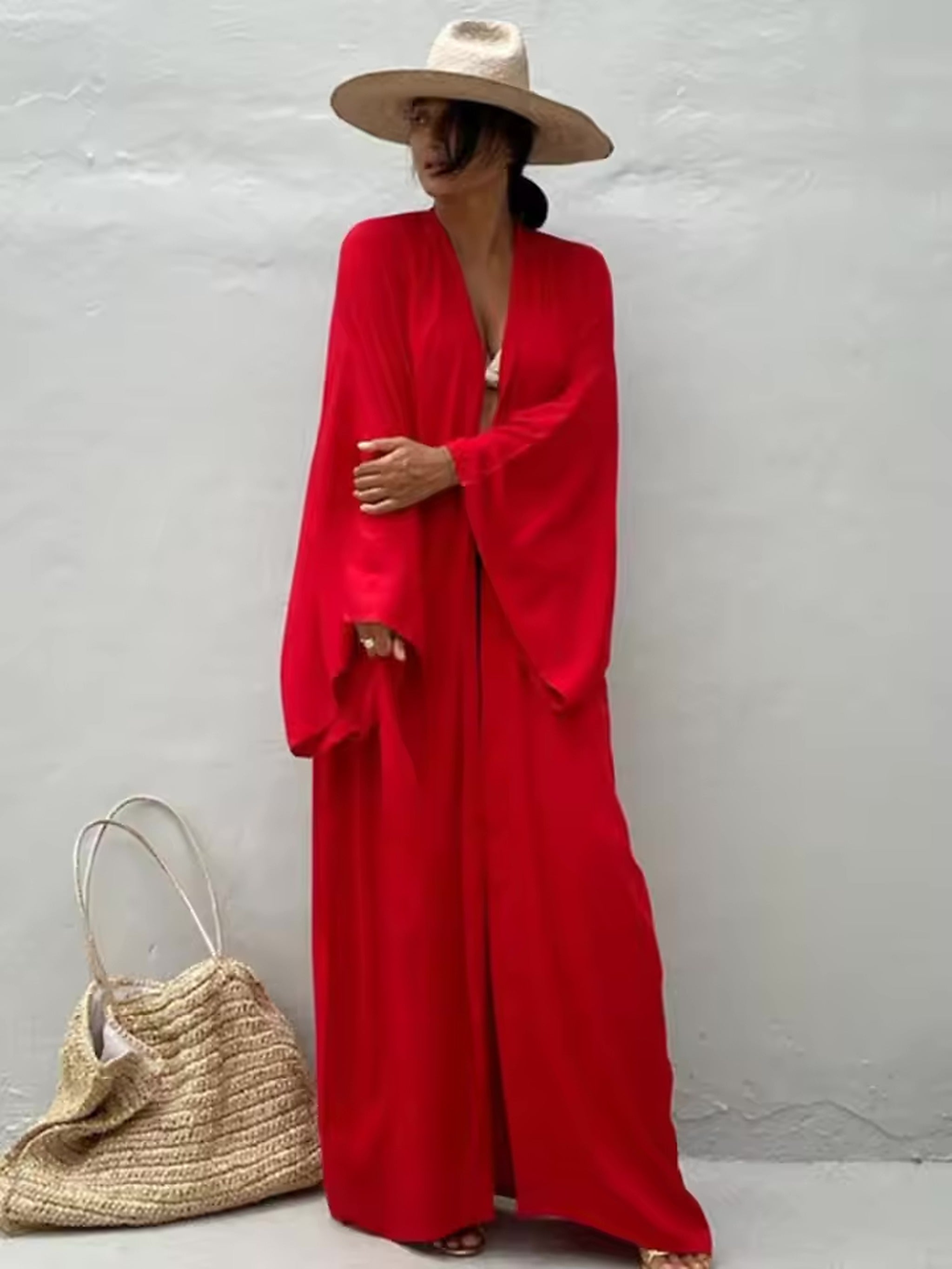 Woman wearing red Luna Mare cover-up with straw hat and woven beach bag by white wall