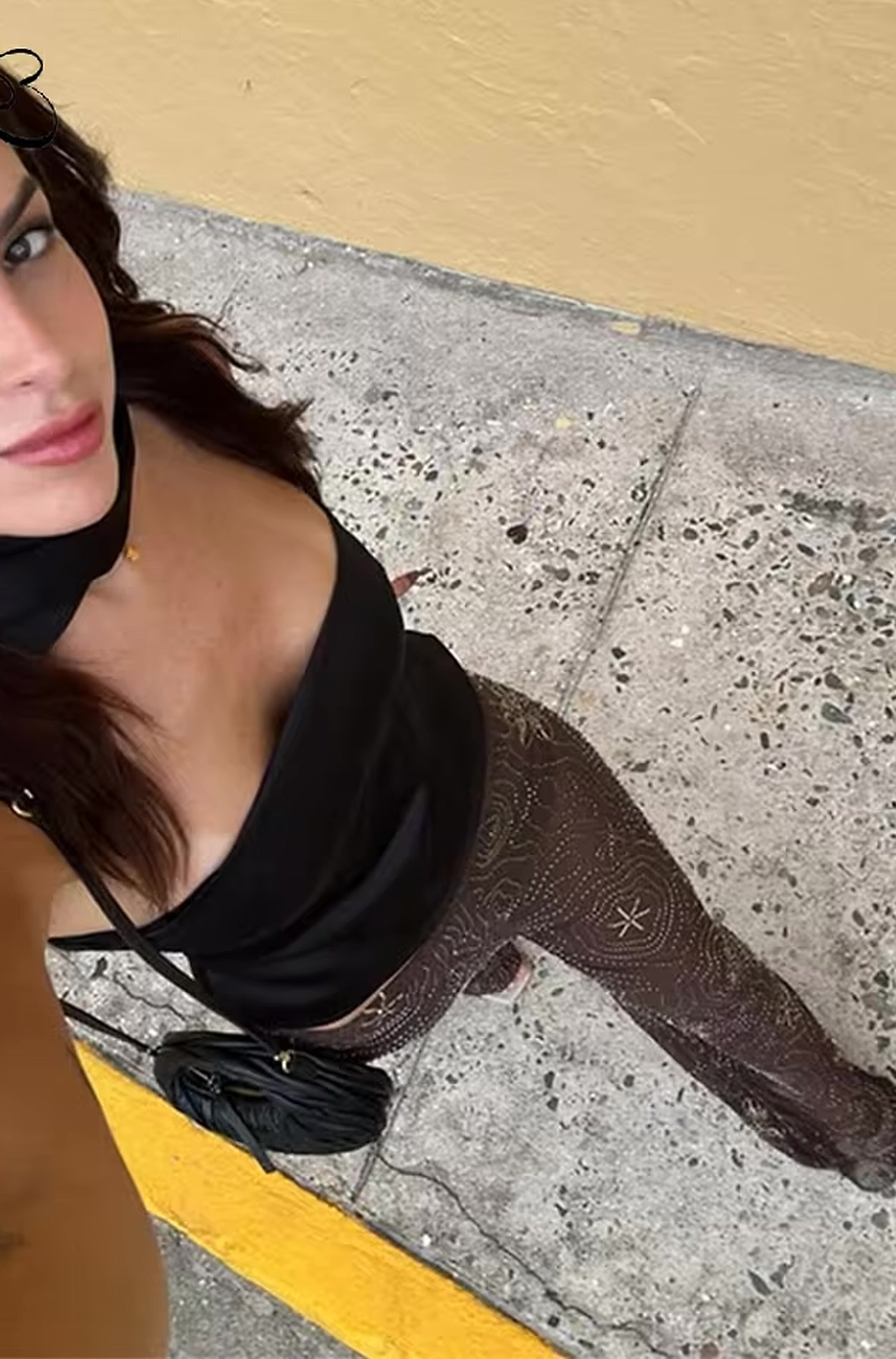 Woman wearing black Noir Sunset pants by poolside with yellow and concrete backdrop