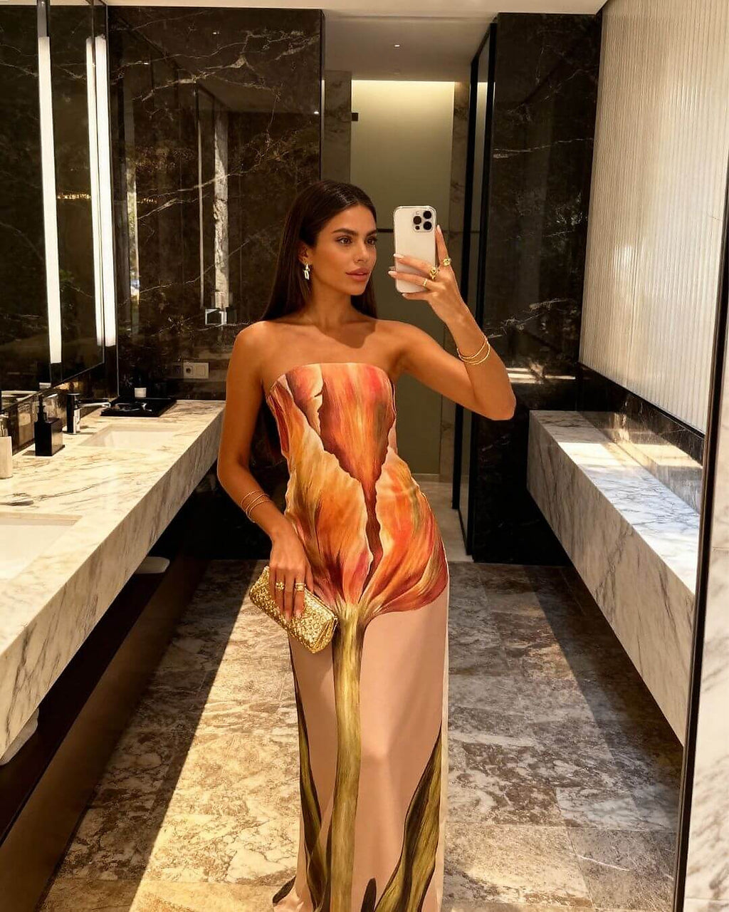 Woman wearing coral and gold strapless cover-up dress with flame print pattern in luxury bathroom mirror setting.