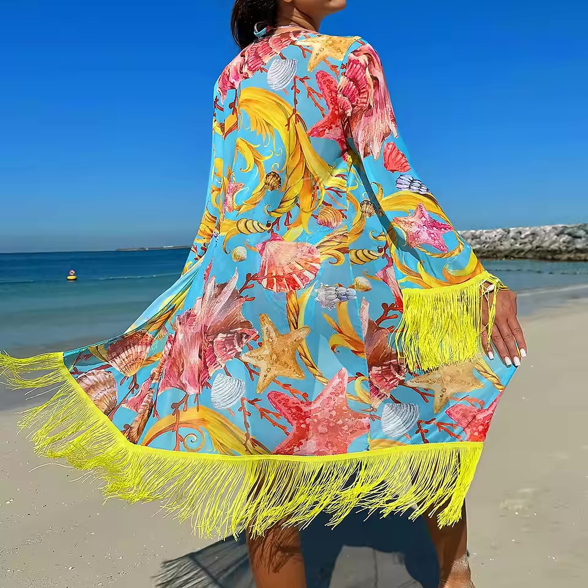 Woman wearing colorful tropical print bikini cover-up with yellow fringe trim, seashell and starfish pattern on blue