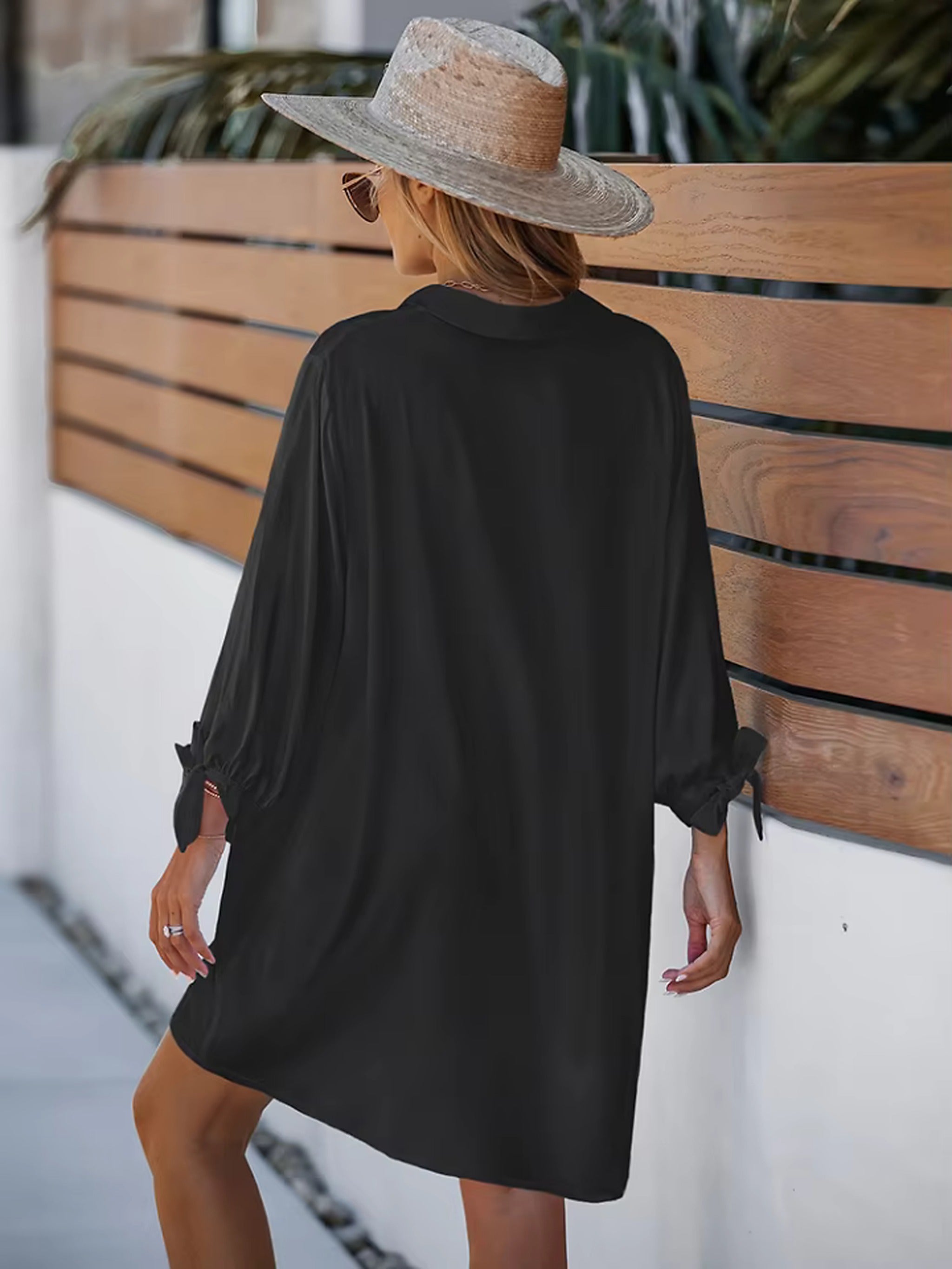 Woman wearing black beach cover-up shirt over bikini, styled with straw hat and sunglasses