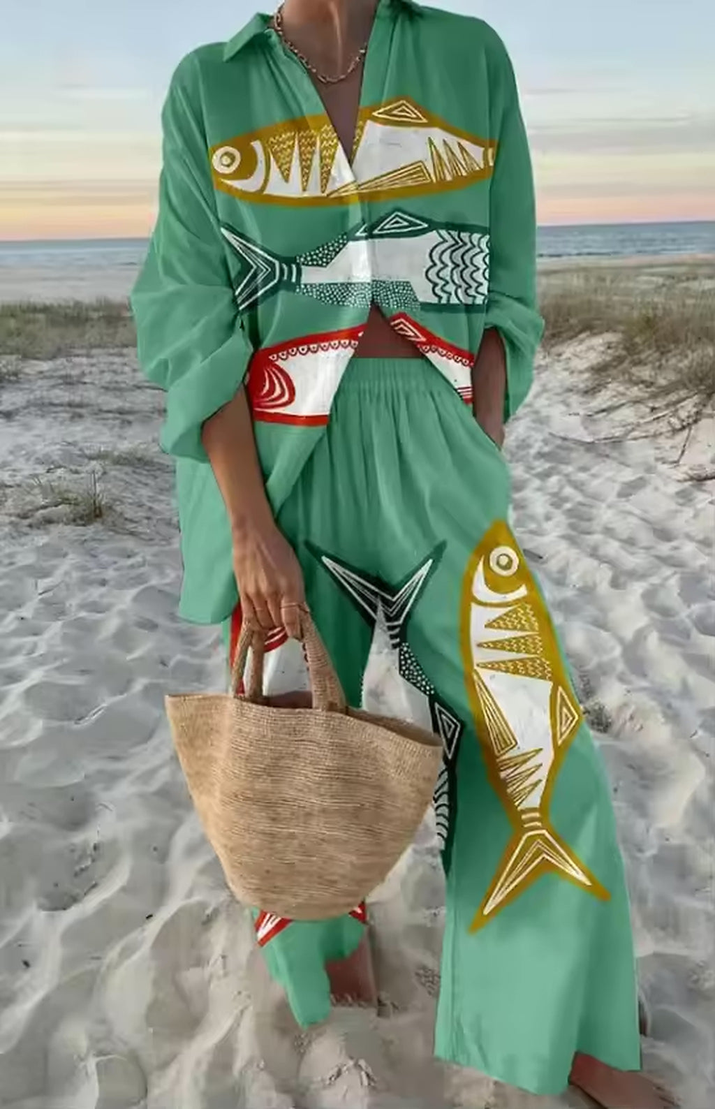 Green fish-print bikini with matching cover-up on model at beach with straw bag